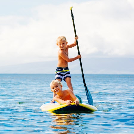 2 boys playing on a stand up paddle board
